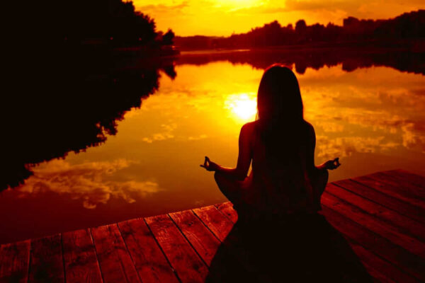 A Girl Is Sitting Near The Water In A Yoga Posture During Sunset